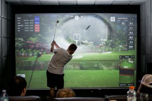 Person playing virtual golf on a large indoor simulator screen.