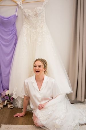 Wedding dress and purple bridesmaid dress hanging in preparation room.