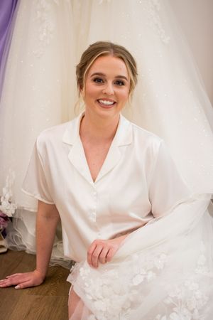 A person in a white silk robe sits against a backdrop of white tulle and purple accents.