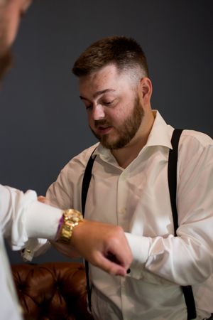 Groomsman in white shirt and suspenders preparing for wedding ceremony.