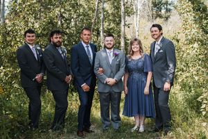 Wedding party poses for formal photo in mix of navy suits and blue dresses against autumn foliage.