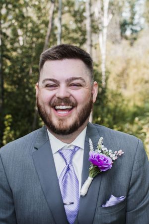 Groom wearing gray suit with purple tie and floral boutonniere.