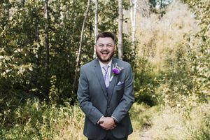 Groomsmen in gray suits pose outdoors against a natural backdrop.