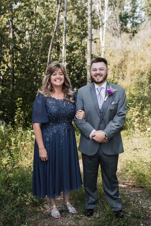 A couple poses in navy blue and gray formal attire for a series of outdoor wedding photos in a wooded setting.