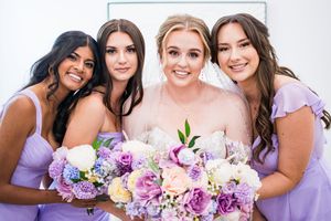 Bridal party in lavender dresses holding colorful bouquets against white background.