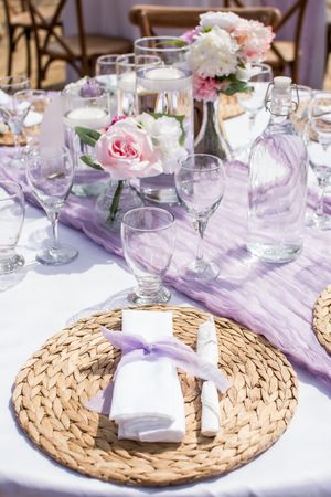 Elegant table settings with woven placemats, purple accents, and floral centerpieces at a wedding reception.