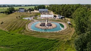 Aerial panorama of wedding venue with circular pond and landscaped grounds.