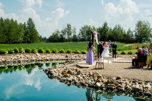 Wedding ceremony taking place on a wooden platform beside a reflective pond with stone edges.