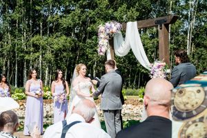 Outdoor wedding ceremony with wooden benches and trees in background.