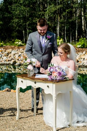 Wedding ceremony couple signing documents at an elegant white desk outdoors.