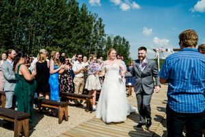 Wedding guests gather outdoors for celebration under bright blue sky with trees in background.