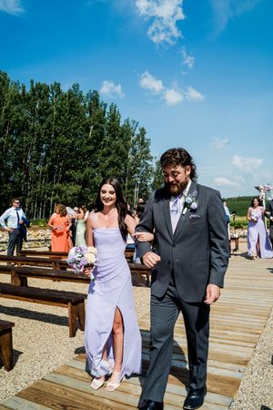 Wedding party members walking on a wooden deck under bright blue skies during an outdoor celebration.