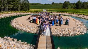 Panoramic view of outdoor wedding venue with wooden deck overlooking lake and rocky shoreline.