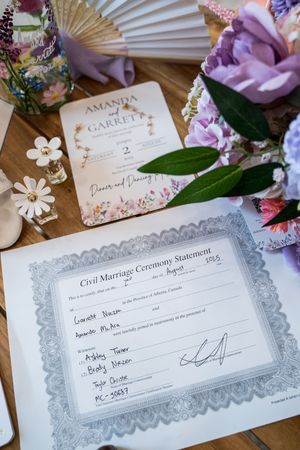 Wedding invitation and marriage certificate displayed with pink flowers and decorative fan.