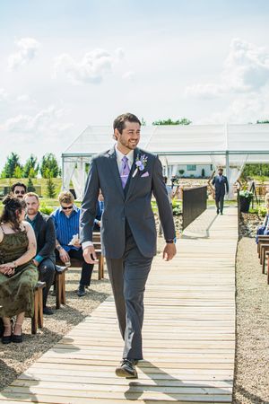 Wedding processional on a wooden walkway with guests seated on both sides under sunny skies.