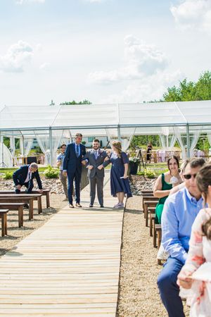 Outdoor wedding ceremony setup with wooden walkway and white tent in natural setting.