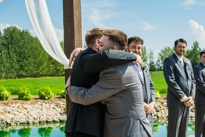 Outdoor wedding ceremony with guests embracing under white drapes and blue sky.
