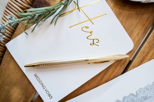 Wedding stationery with gold pen and olive branch on wooden table features elegant calligraphy and white paper.