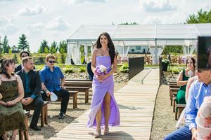 Outdoor wedding ceremony setup with purple decor and wooden benches.