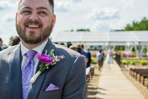 A boutonniere with purple flowers adorns a grey suit jacket.