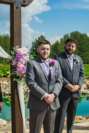 Groomsmen lined up at outdoor ceremony venue with turquoise pond in background.