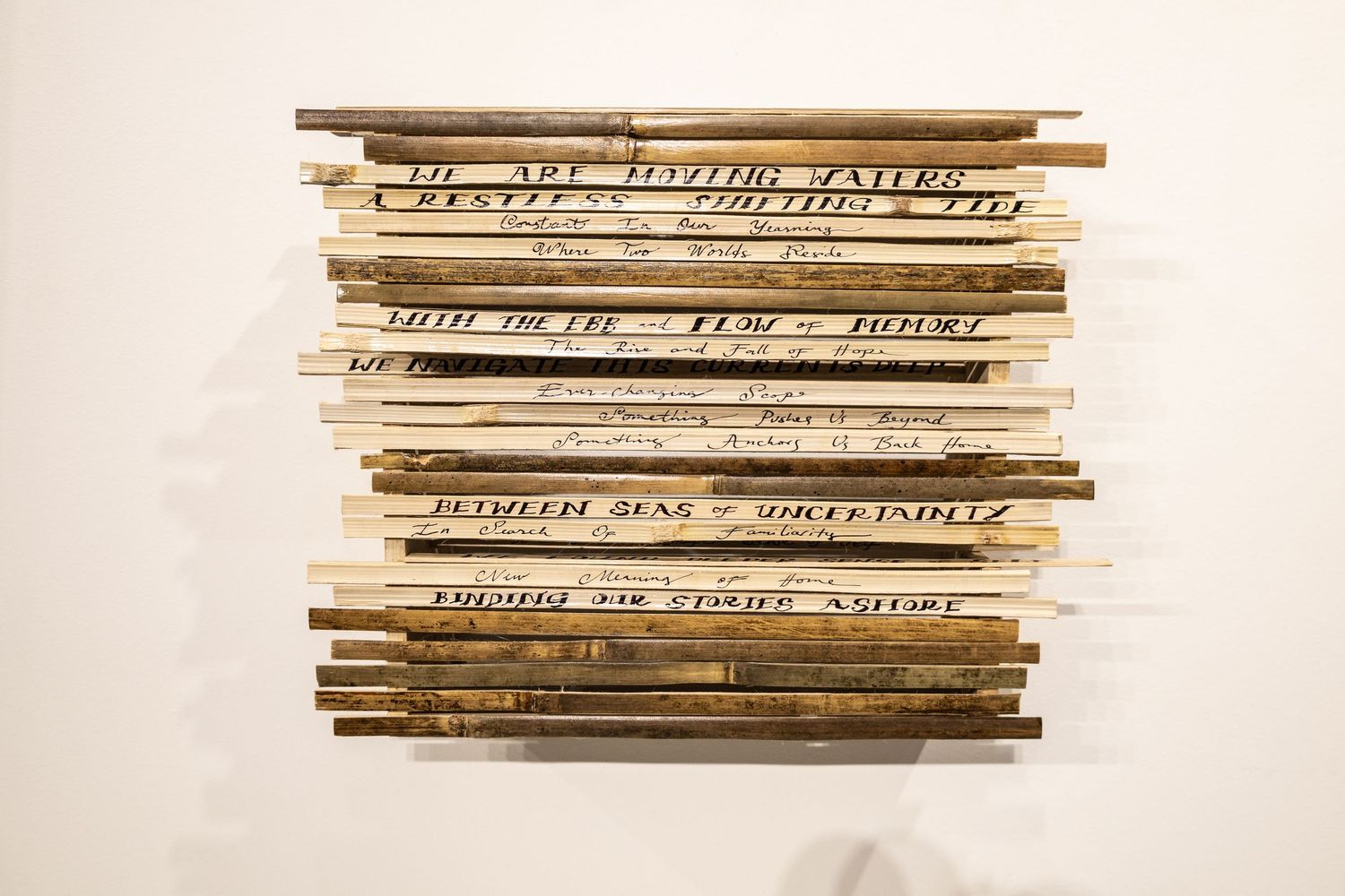 Wooden sticks with handwritten text arranged in horizontal rows as a wall art installation.