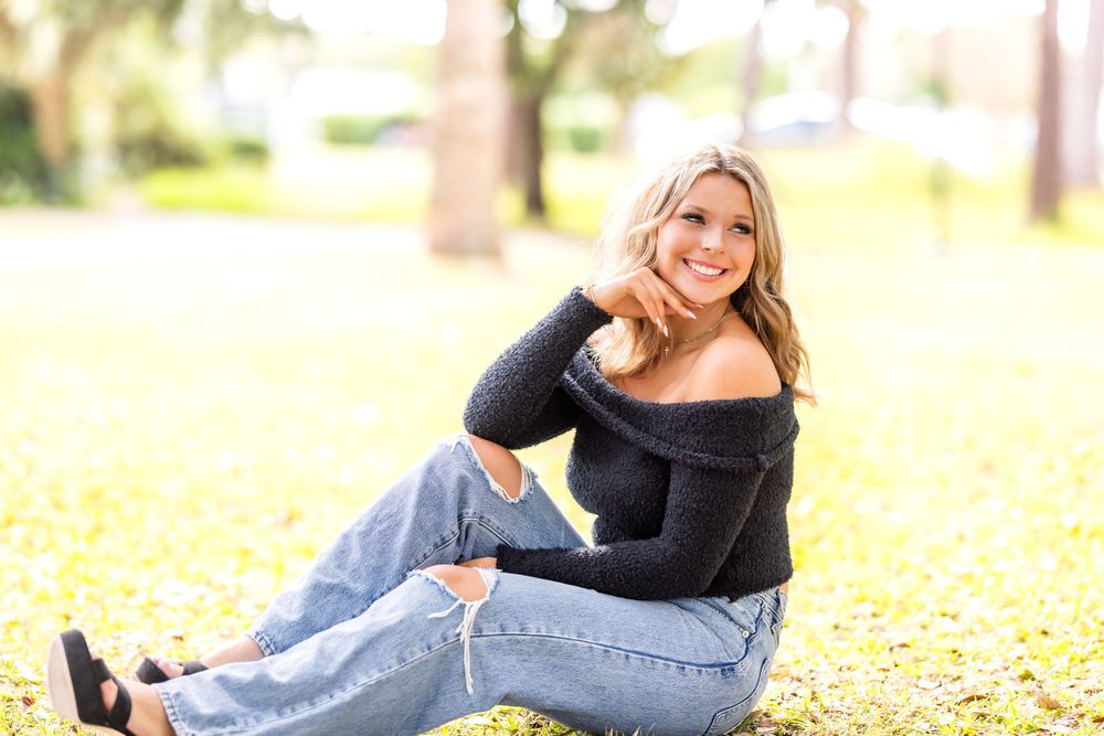 A person in a black sweater and jeans lies on autumn leaves during an outdoor portrait photography session.