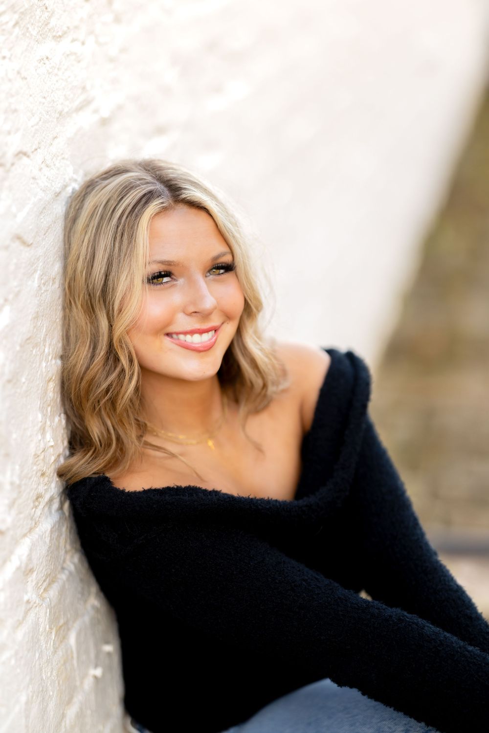 A woman in a black sweater poses against a light colored wall in a series of casual portraits.