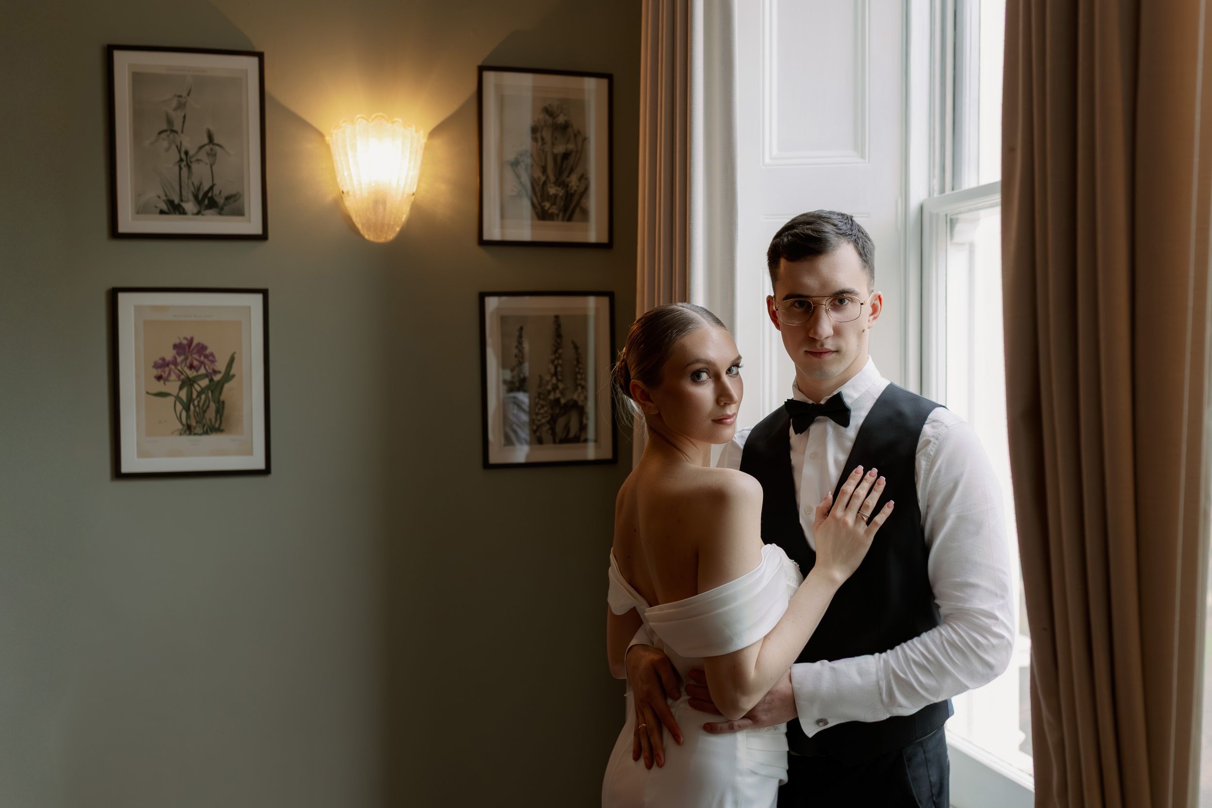 A couple dances together in an elegant room with soft window light and framed artwork on the walls.