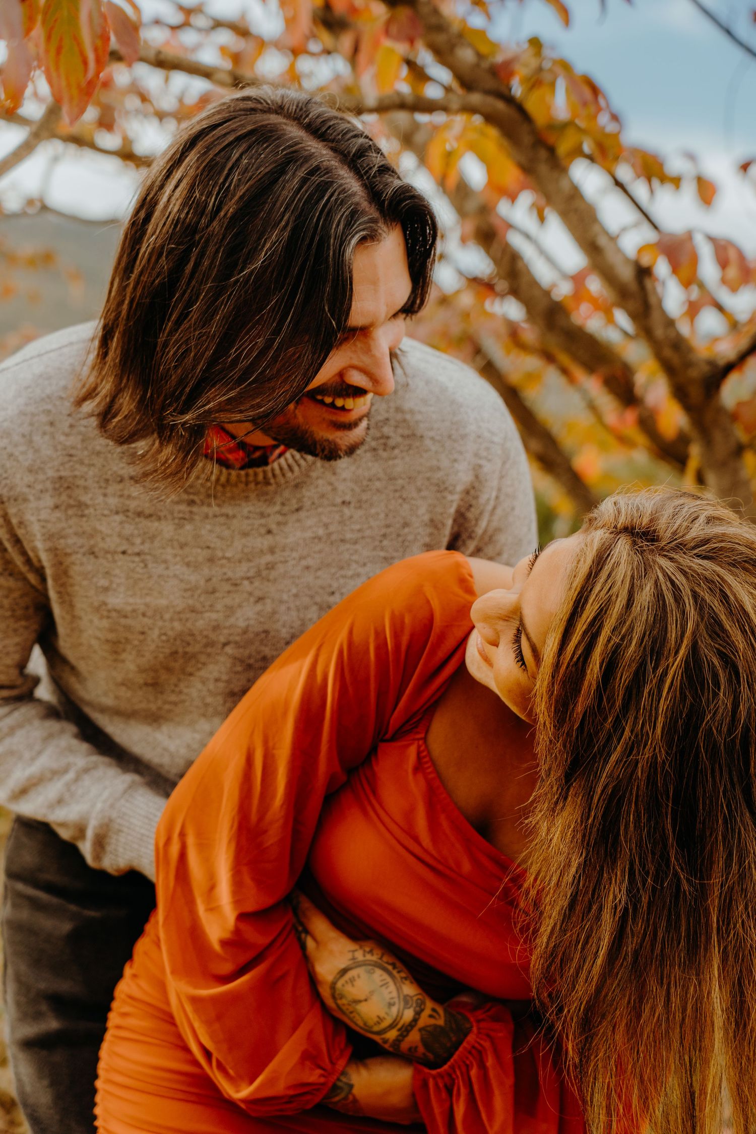 Couple sharing an intimate autumn moment among orange fall foliage in warm sweaters.