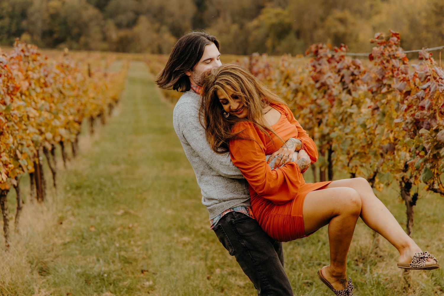 Playful moment between couple in vineyard with fall colors and mountains in background.