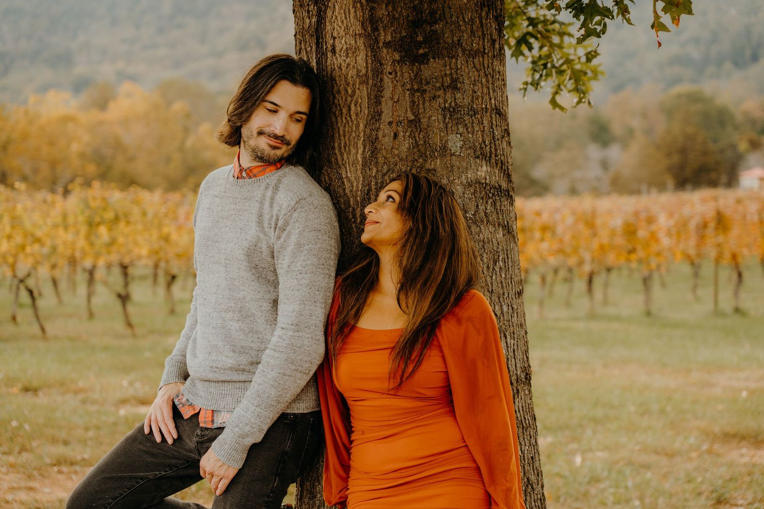 Joyful autumn portrait against tree trunk with vineyard in background.