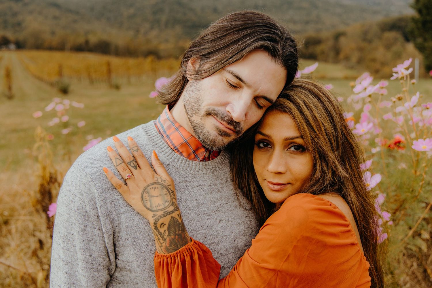 Couple embraces in a golden field during sunset with mountains in the background.