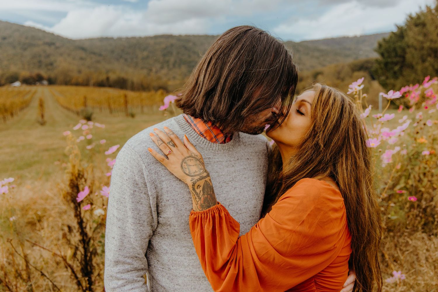 Couple embracing in an autumn field with mountains in the background.
