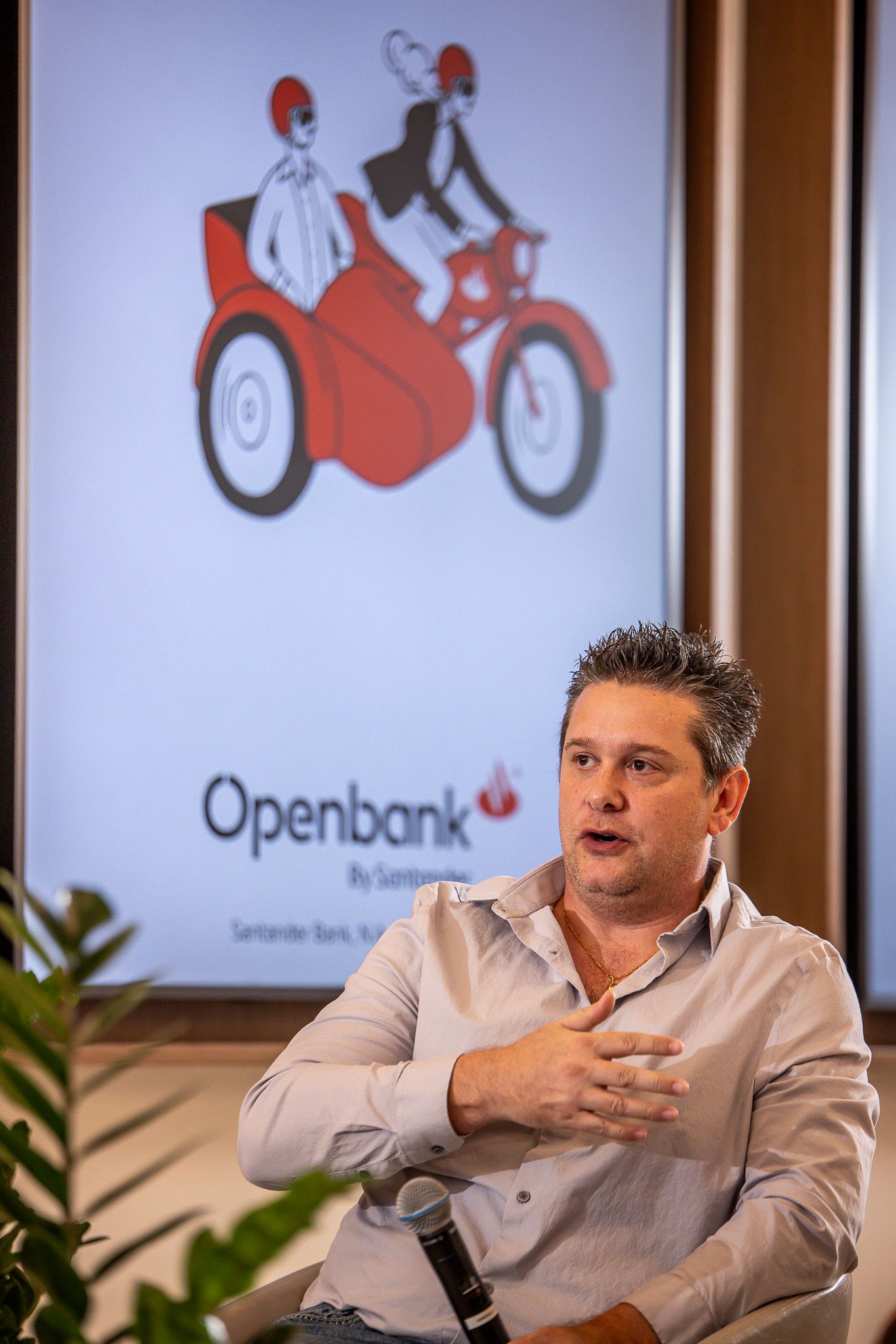 A person speaks during a business presentation with an Openbank logo showing a red and white motorcycle illustration behind them.