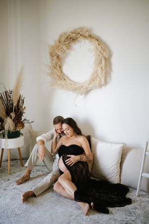 Romantic couple lounging on floor with minimalist decor and dried pampas grass wreath on wall.