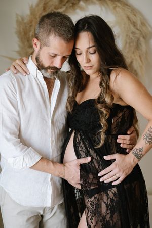 Romantic couple embraces in intimate maternity photos wearing black lace and white shirt.