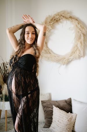 Maternity boudoir session featuring black lace robe against white wall with dried pampas grass decor.