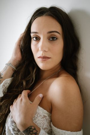 A woman with dark hair poses in a white off-shoulder dress in a series of romantic boudoir portraits.
