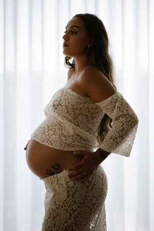 Artistic maternity silhouettes showcasing a lace dress in natural window light.