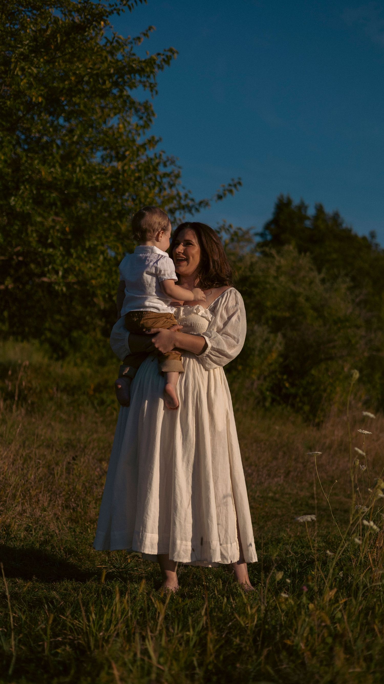 Two people in white dresses embrace lovingly in a sunlit meadow at golden hour.