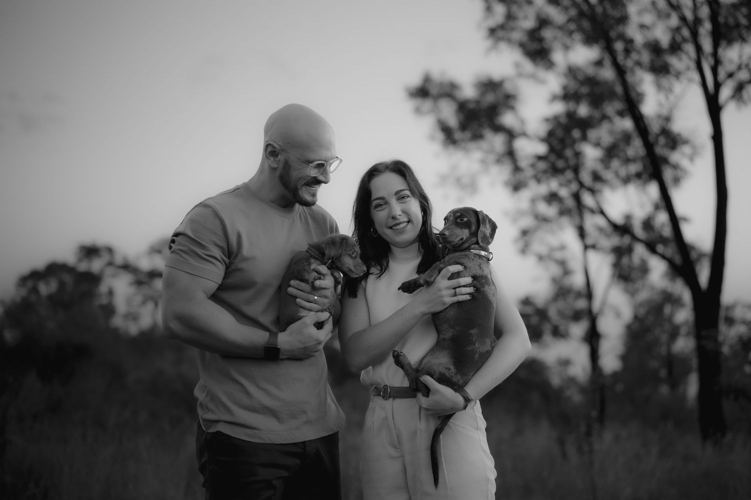 A black and white family portrait with a couple holding their dogs outdoors.