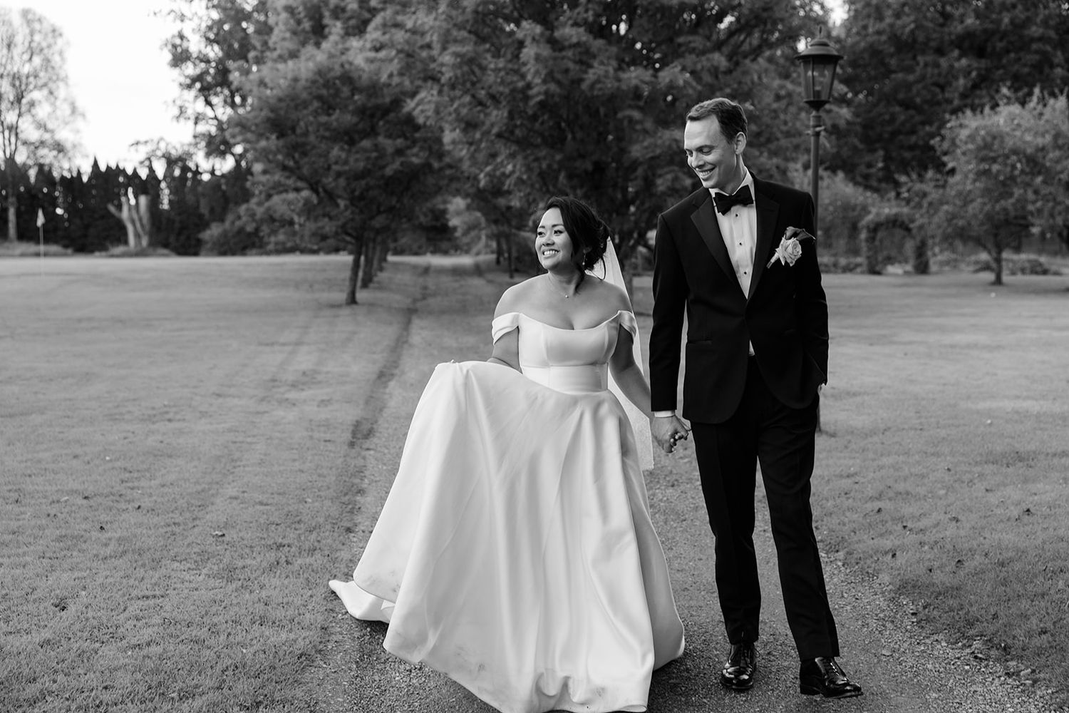 A couple in formal wedding attire walks together through a scenic outdoor setting on their special day.