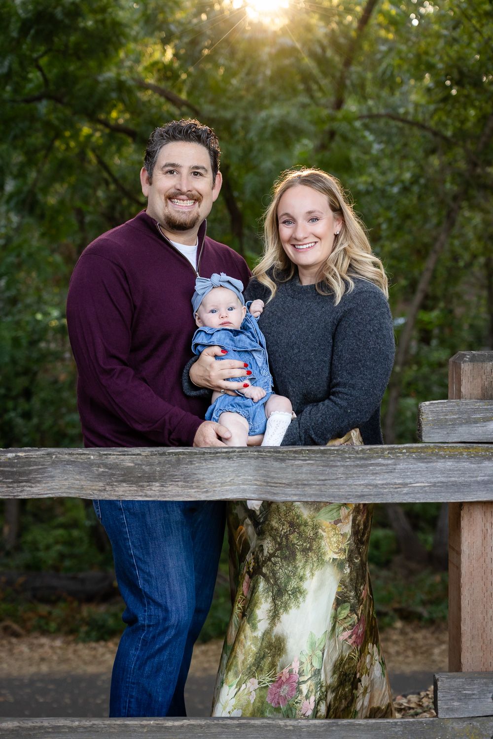 A San Jose couple poses with their baby along wooden fence at sunset in outdoor autumn portrait session