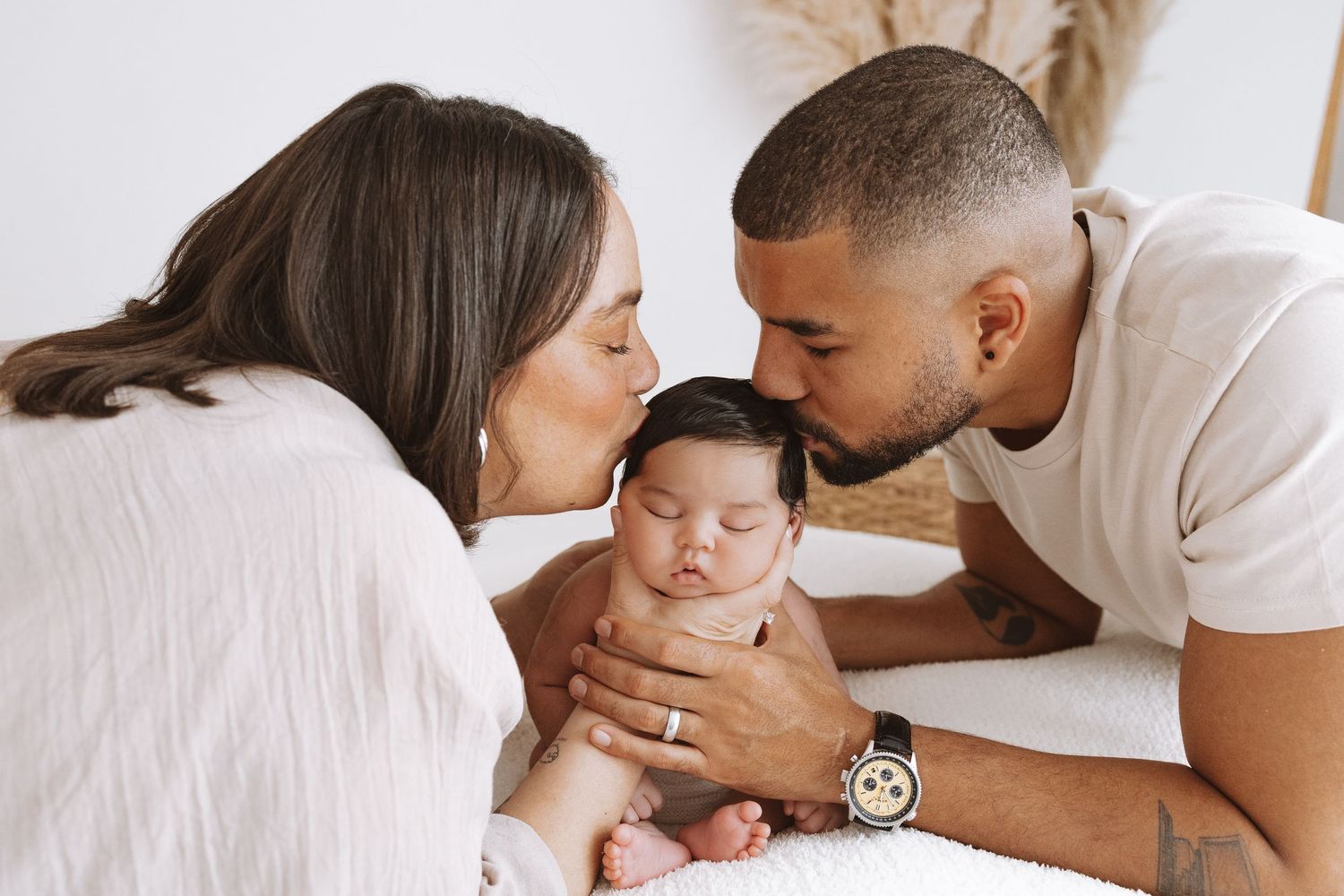 A tender family moment captured in white tones as parents share affectionate moments with their baby on a bed.