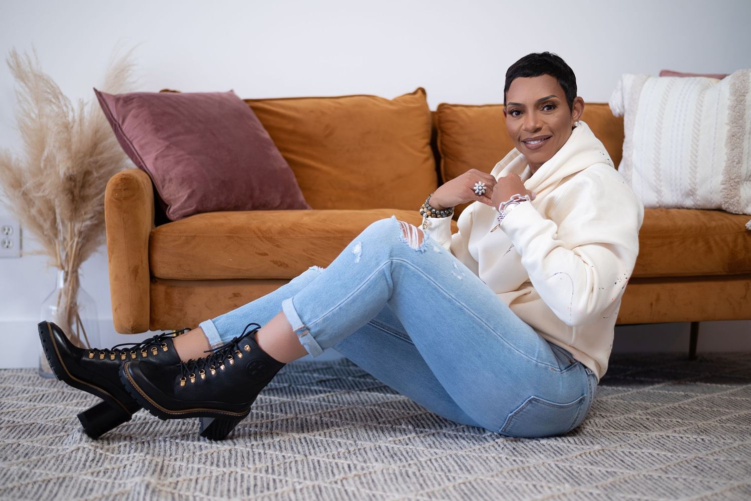 Person in light blue jeans and black boots lying on floor against orange couch and gray carpet.
