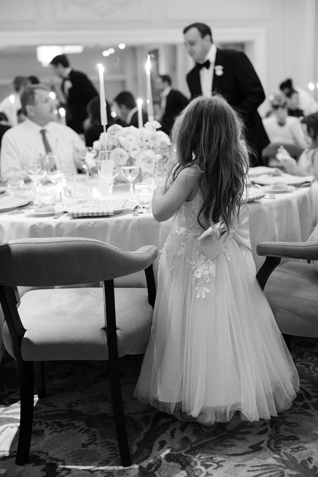 Young children in white dresses play and dance at an elegant wedding reception with tables and decorations.