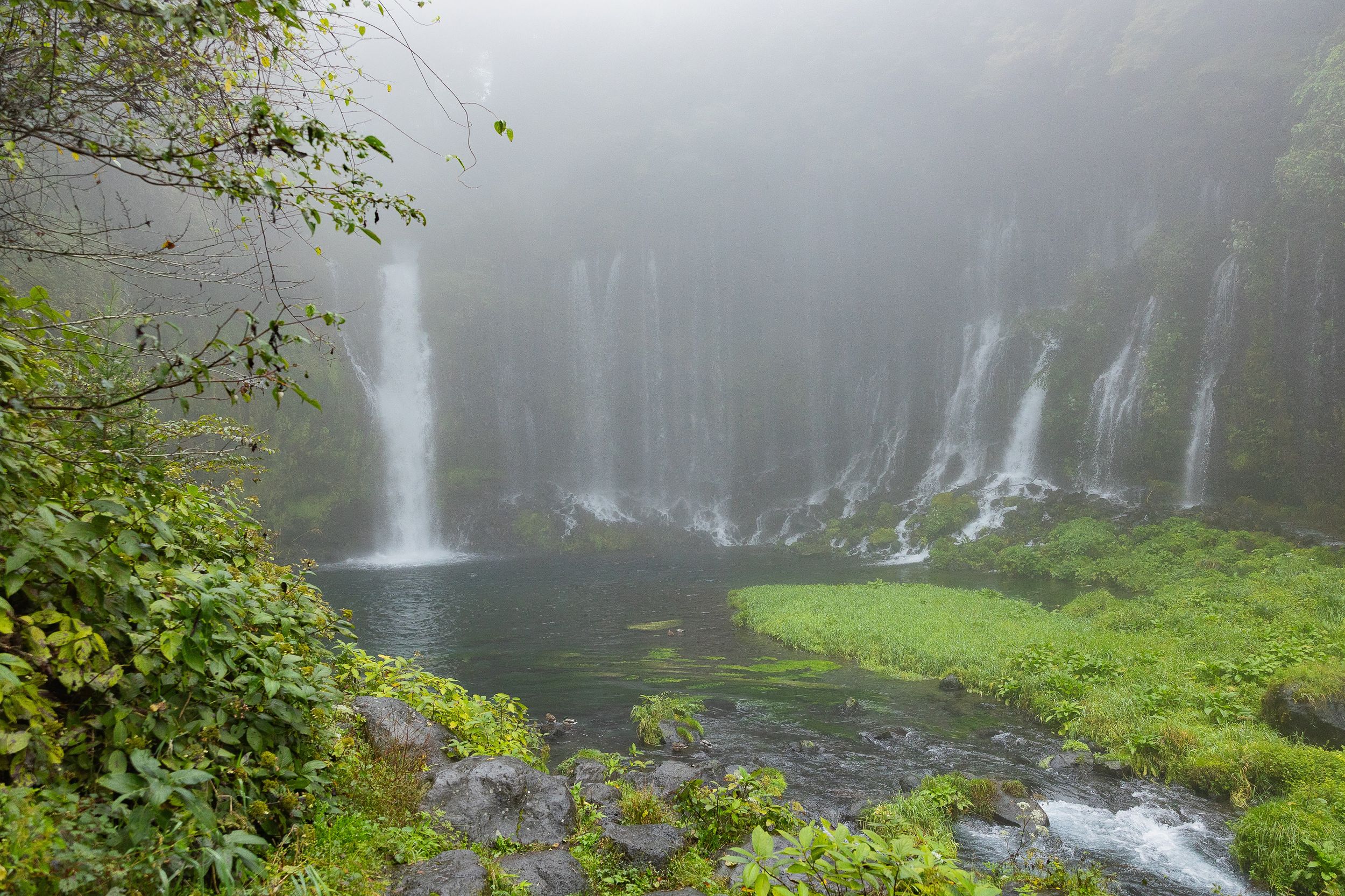 Misty waterfalls cascade down lush green cliffs in a tropical rainforest setting creating a serene natural landscape.