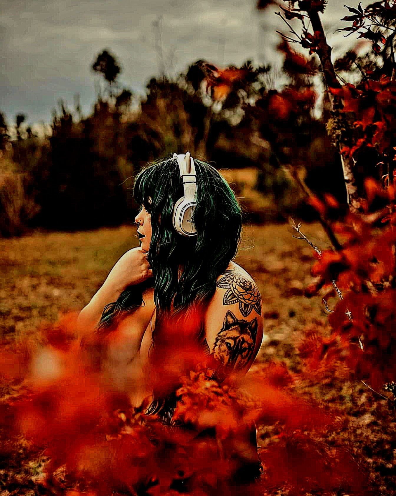 A person with dark hair sits among vibrant red autumn foliage in an outdoor setting during golden hour.