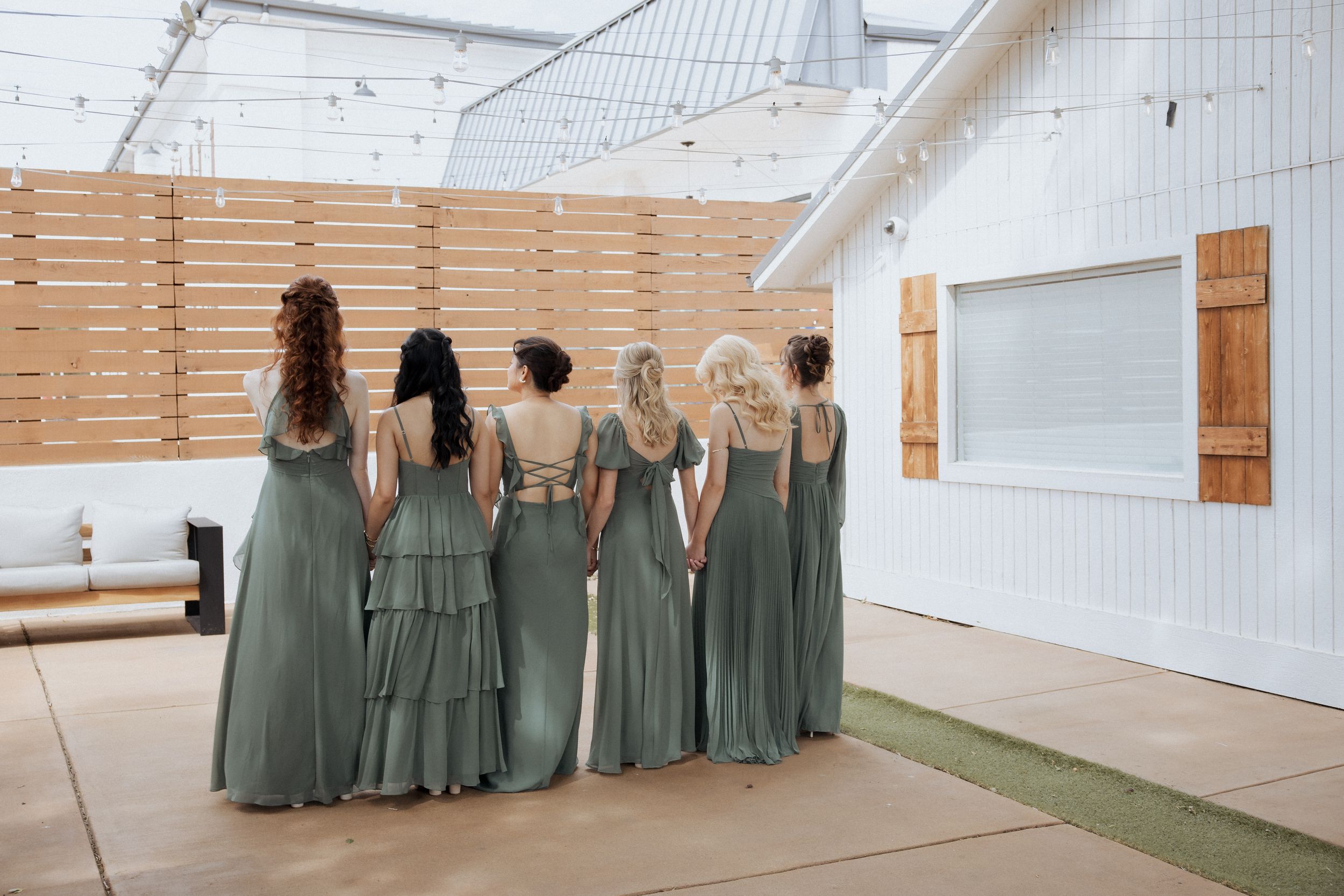A group wearing sage green dresses stands in a row against a white wall with wooden accents.